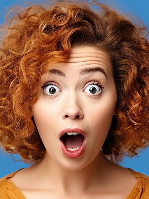 Eine junge Frau mit roten, lockigen Haaren schaut erstaunt in die Kamera.