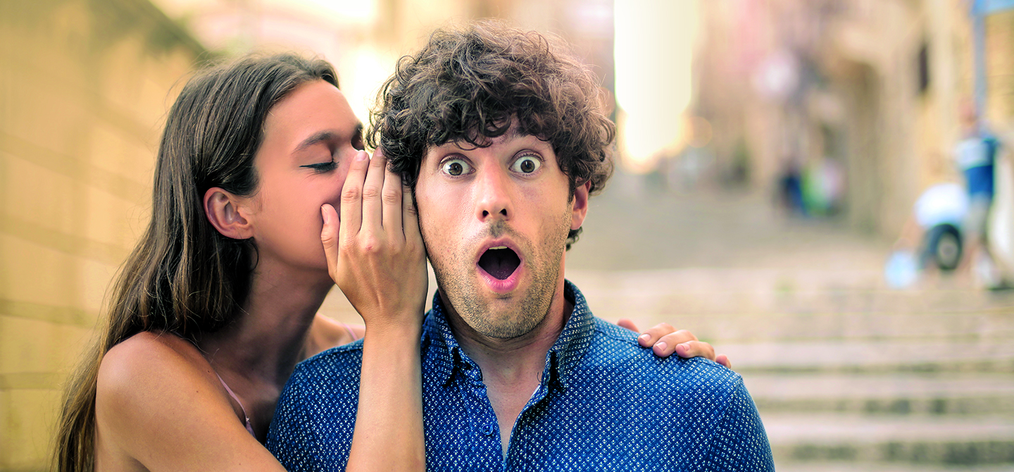 Eine junge Frau flüstert einem jungen Mann ein Geheimnis ins Ohr.