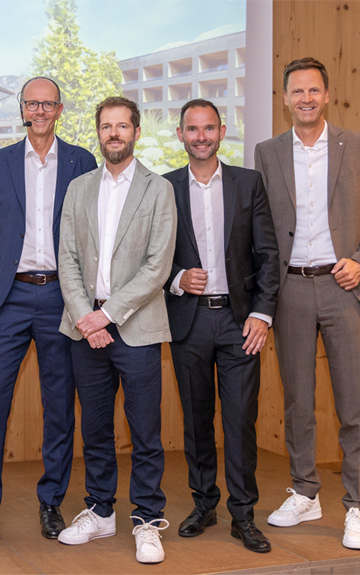 Vier Männer stehen beim Volksbank Tirol Anlage-Gipfel vor einer Präsentationsfläche mit der Aufschrift „Herzlich willkommen zum Anlage-Gipfel“. Fotocredit: DieFotografen