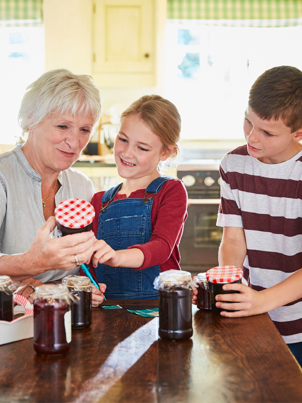 Eine ältere Frau kocht mit ihren beiden Enkelkindern Marmelade ein.