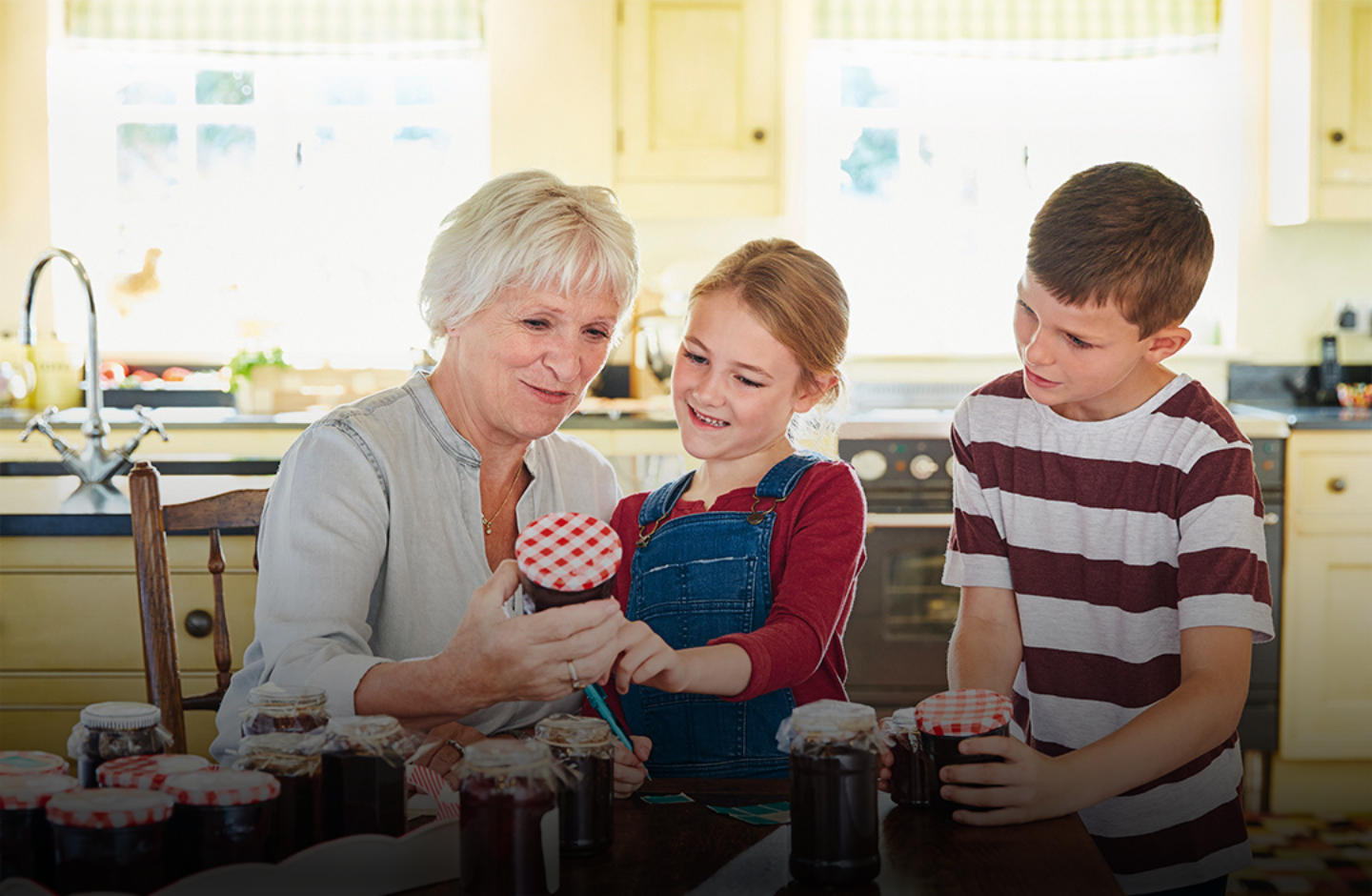 Eine Oma zeigt ihren zwei Enkeln ein Glas Marmelade in einer Küche.