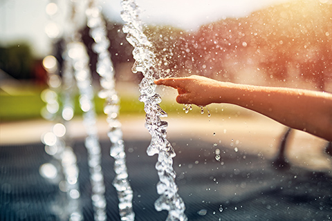 Eine Hand wird in den Wasserstrahl einer Wasserinstallation am Boden gehalten.