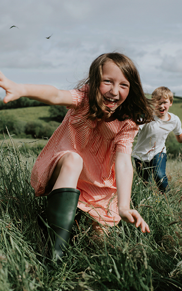 Ein Mädchen und ein Bub laufen über ein Feld auf die Kamera zu. Sie sind ausgelassen und lachen.