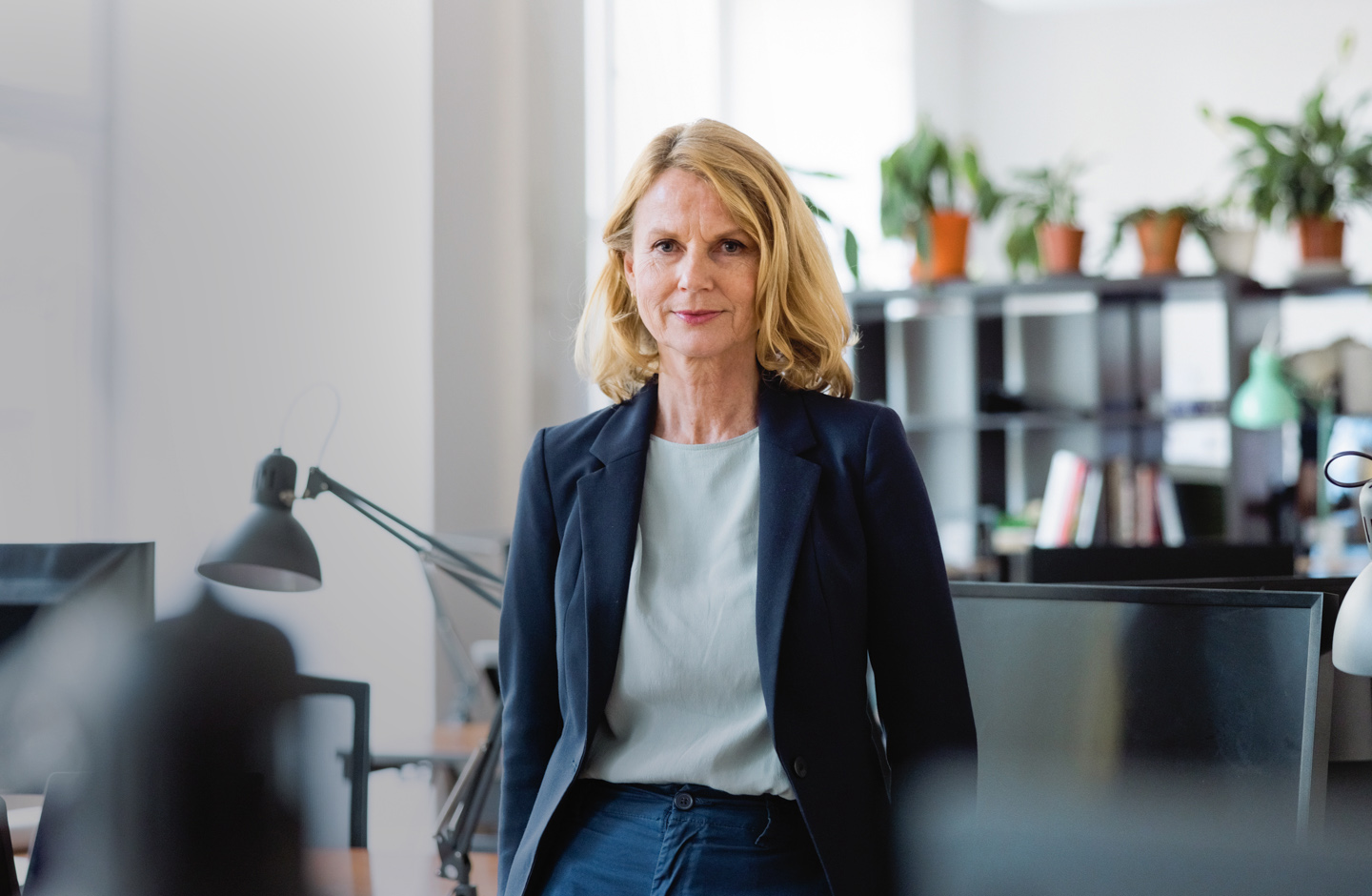 Eine Unternehmerin steht in ihrem Büro. Sie blickt direkt in die Kamera.