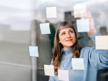 Eine Frau steht hinter einer Glasscheibe und klebt Post-Its an diese.