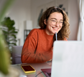 Eine Frau sitzt an ihrem Schreibtisch vor einem Notebook. Sie hat die Augen geschlossen und lächelt.