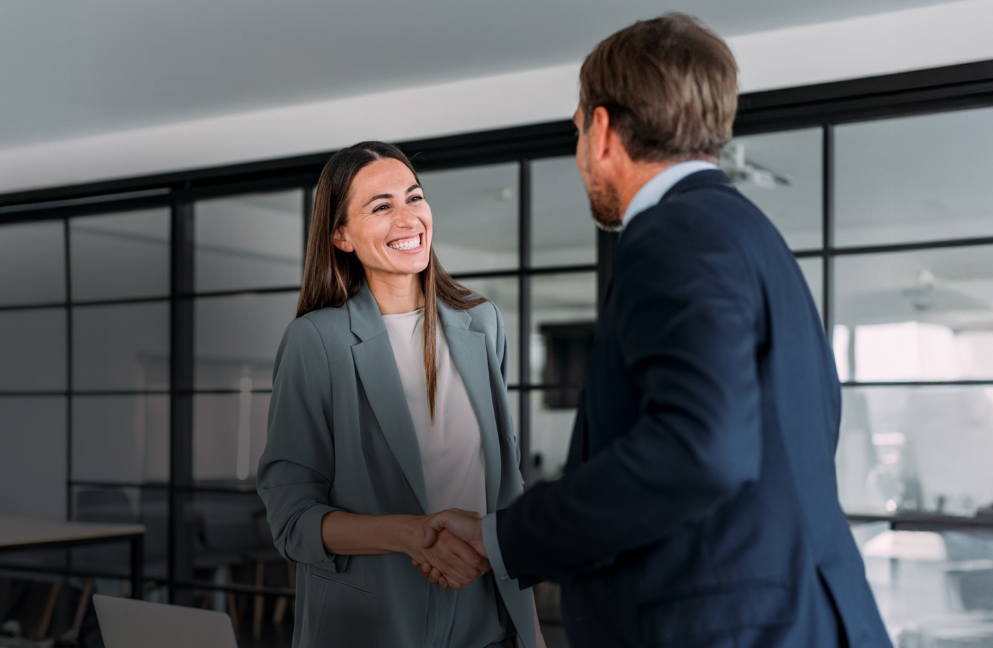 In einem Büro schüttelt eine Frau im Blazer einem Mann im Anzug die Hand.